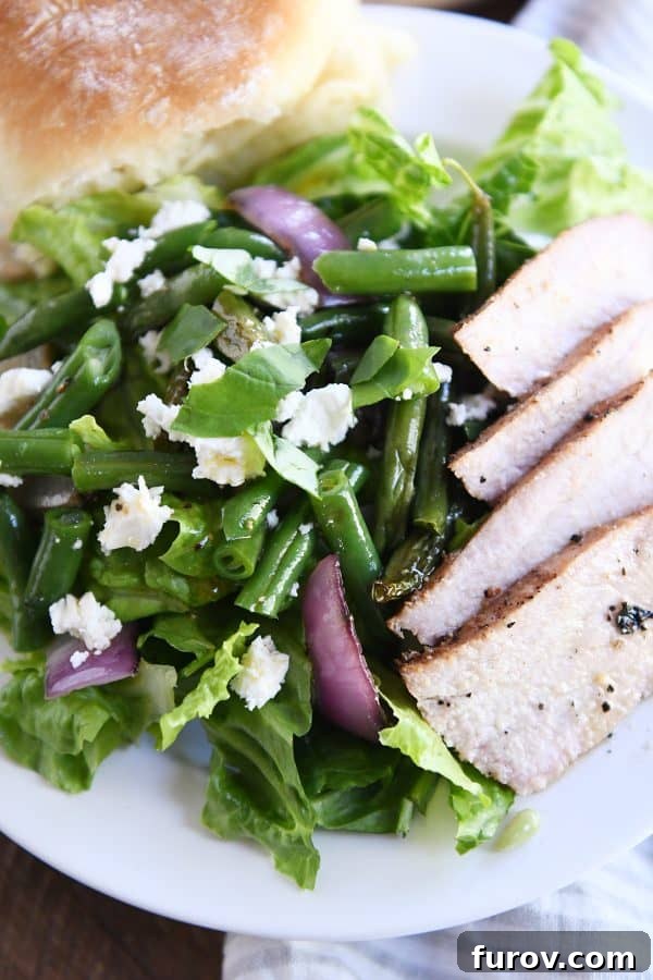 A vibrant grilled pork and veggie salad served on a white plate, featuring romaine, grilled onions, and feta cheese.