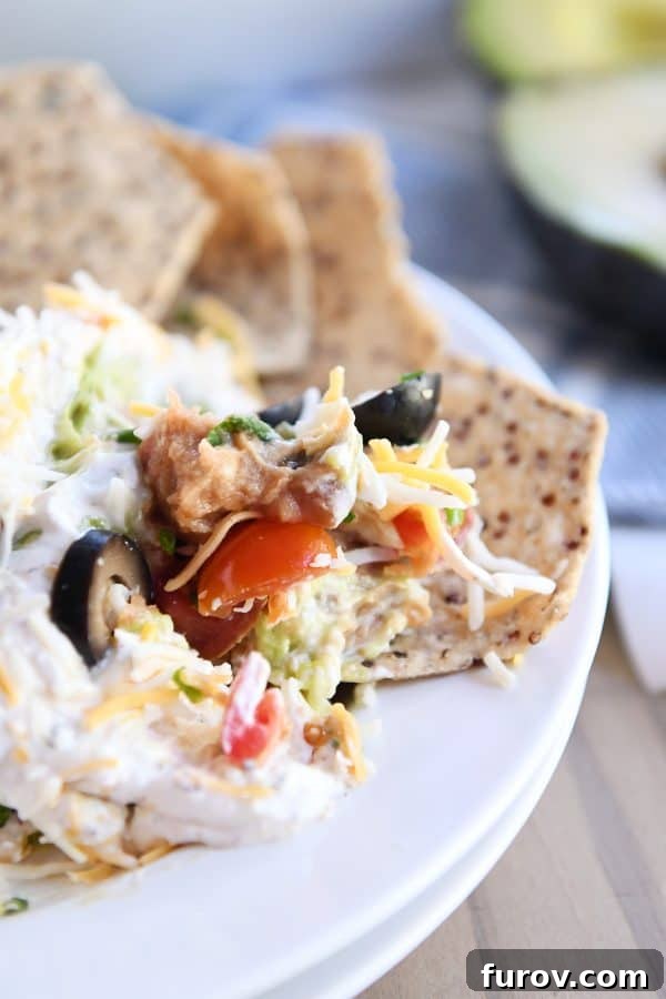 A generous scoop of 7-layer dip served on a multigrain tortilla chip, ready to be enjoyed.