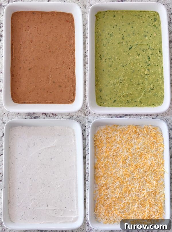 The initial layers of refried beans, guacamole, sour cream, and shredded cheese visible in a white dish, building the foundation of the 7-layer dip.