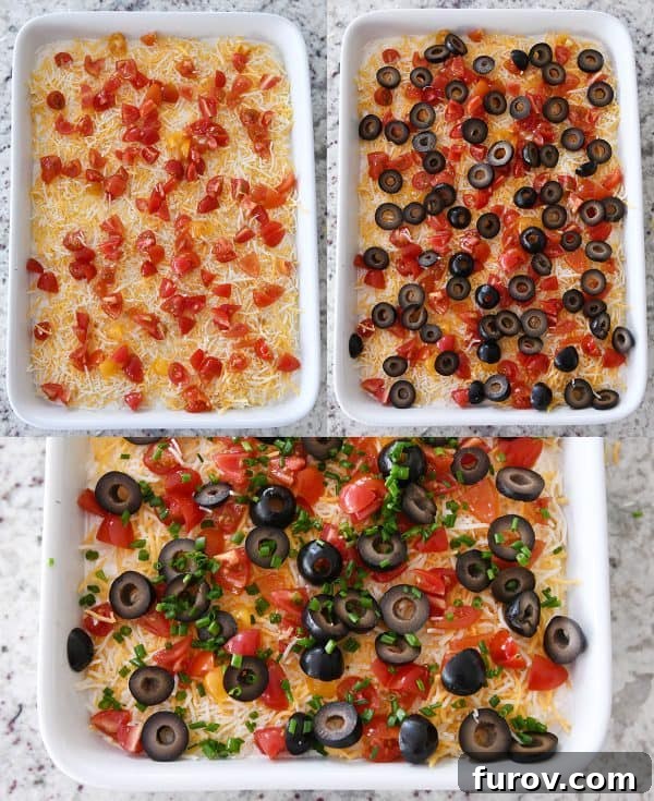 The top layers of chopped tomatoes, sliced olives, and green onions adorning the 7-layer dip in a pristine white dish.