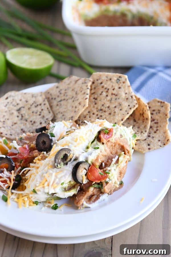 A big scoop of 7-layer dip on a white plate, accompanied by crunchy tortilla chips, showcasing its vibrant layers.