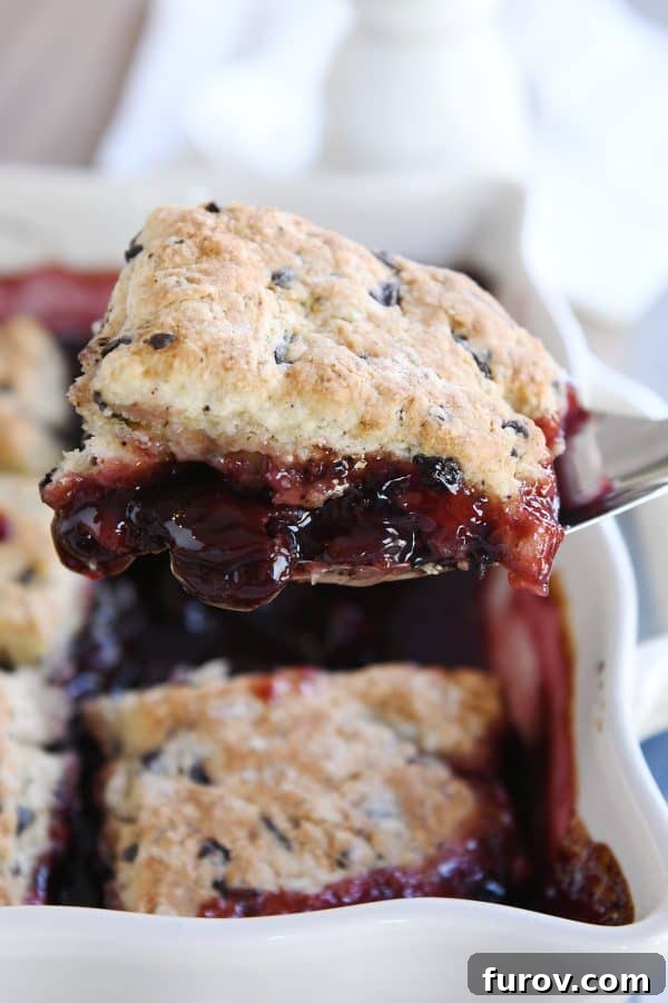 Lifting scoop of chocolate chunk cherry cobbler out of dish with spatula.