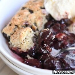 serving of cherry chocolate cobbler with chocolate chunk biscuit and vanilla ice cream in white bowl