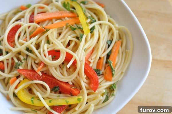 Vibrant Asian Noodle Salad 3 Top view of a white bowl with cooked spaghetti noodles and sliced peppers.