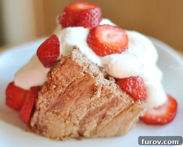 Heavenly Angel Food Cake Classic and Chocolate Flavors 3 Slice of angel food cake with whipped cream and sliced strawberries on a white plate.