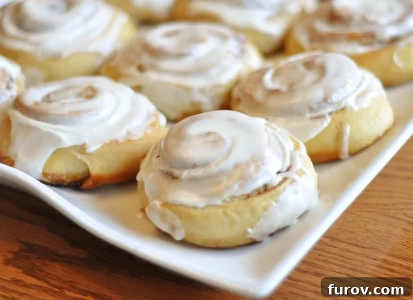 Irresistible Buttermilk Cinnamon Rolls with Silky Cream Cheese Frosting 2 A glistening white platter holds a collection of small, elegantly frosted buttermilk cinnamon rolls, their swirls visible beneath a generous layer of cream cheese glaze.