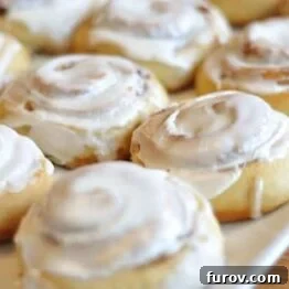 Buttermilk Cinnamon Rolls topped with a smooth, white cream cheese glaze, presented on a light background.