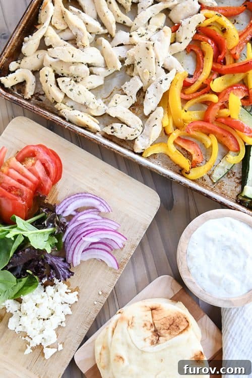 A sheet pan loaded with cooked chicken and colorful bell pepper slices sits beside a cutting board with fresh, sliced vegetables for prep.