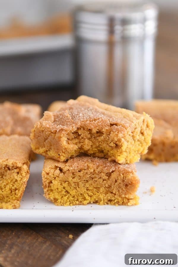 Two soft and scrumptious pumpkin snickerdoodle bars stacked on a white tray, with a bite taken out of the top bar, highlighting their perfect texture.