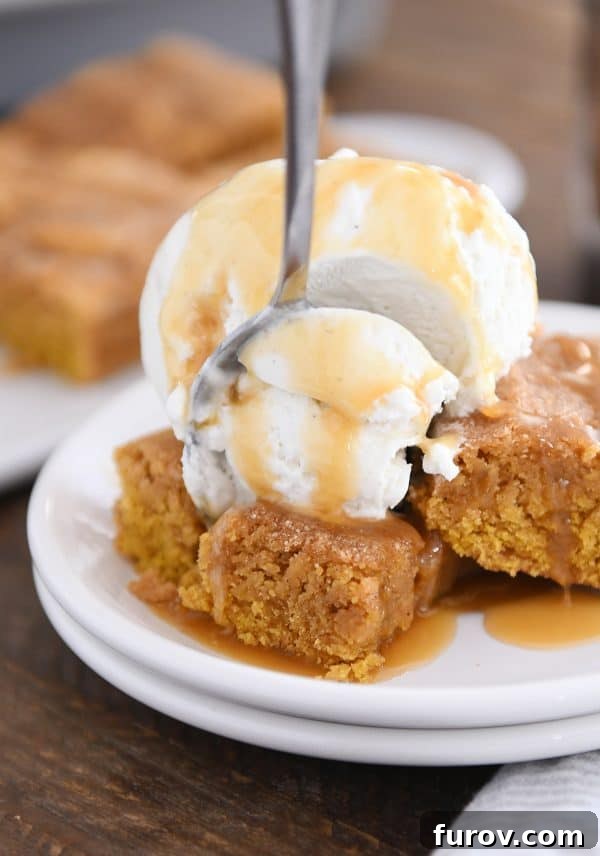 A fork taking a delicious bite out of an easy pumpkin snickerdoodle bar, served on a white plate with a scoop of vanilla ice cream and drizzled butterscotch sauce.