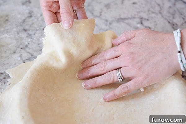 Unlock the Secret to Flaky Homemade Pie Crust 19 A hand gently lifting the edge of a pie crust to fit it perfectly into a pie dish without stretching.