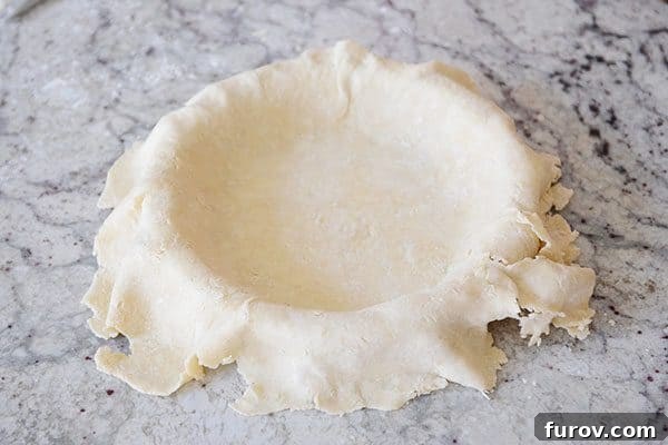 Unlock the Secret to Flaky Homemade Pie Crust 20 An untrimmed, uncooked pie crust beautifully fitted into a pie dish.