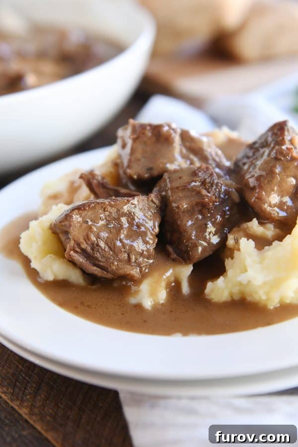 Fall-Apart Tender Slow Cooker Beef in Rich Gravy 2 Slow cooker smothered beef tips and gravy on creamy mashed potatoes, garnished with fresh herbs.