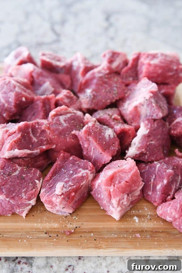 Fall-Apart Tender Slow Cooker Beef in Rich Gravy 5 Raw beef chunks for slow cooker smothered beef tips, perfectly cut on a wooden cutting board.
