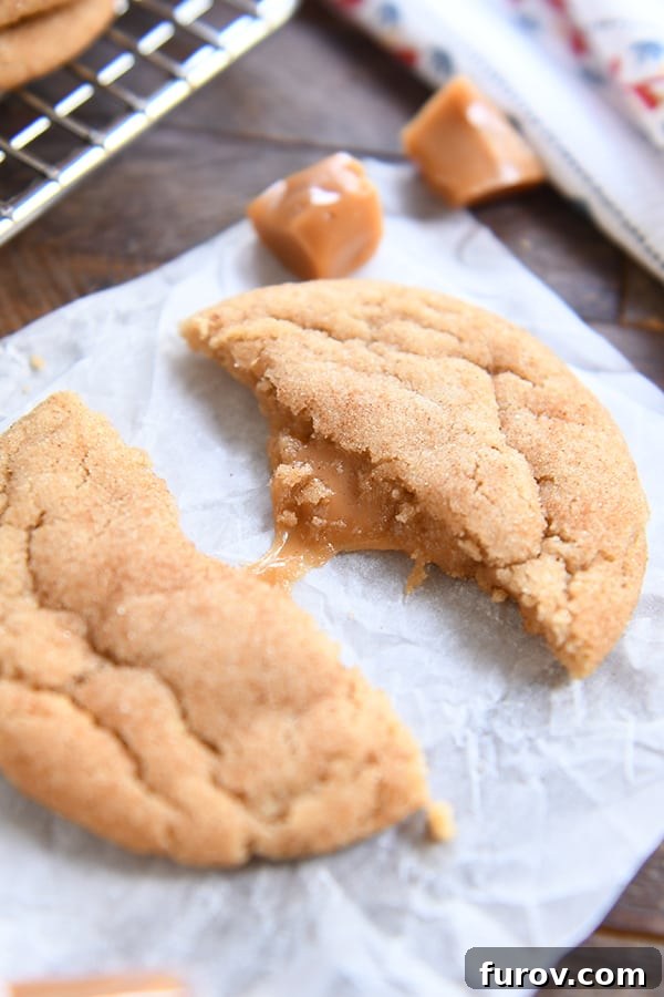 One brown butter caramel snickerdoodle in half pulled apart with caramel stretching on white parchment.