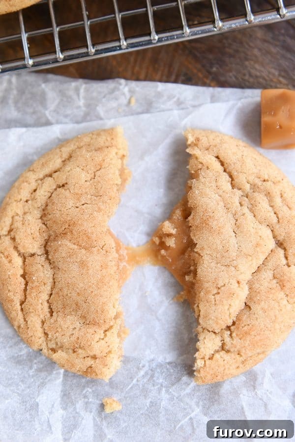 One brown butter caramel snickerdoodle in half pulled apart with caramel stretching on white parchment.