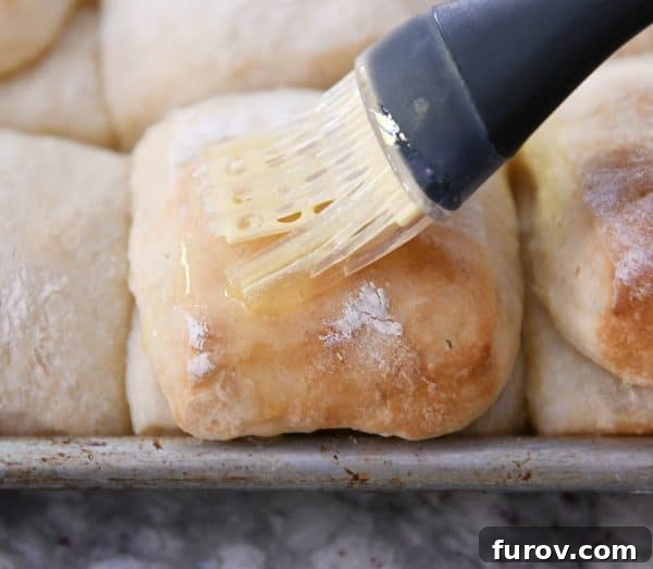 A pastry brush applies melted butter to the warm, golden crust of a freshly baked roll, enhancing its aroma and sheen.