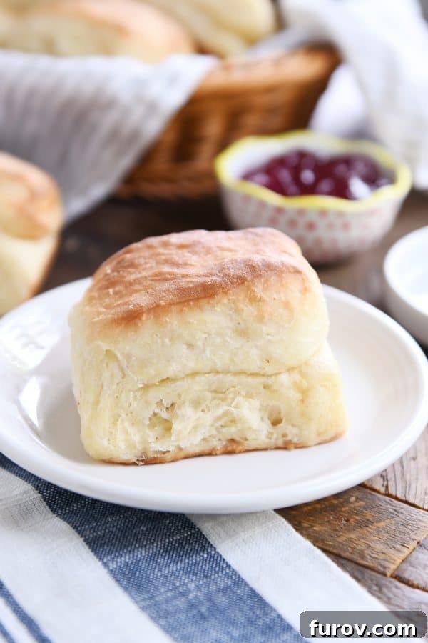 A super fluffy dinner roll presented on a white plate with a decorative white and blue napkin, showcasing its perfect texture.