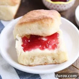 Fluffy dinner roll cut in half and spread with butter and jam, showcasing its soft interior.
