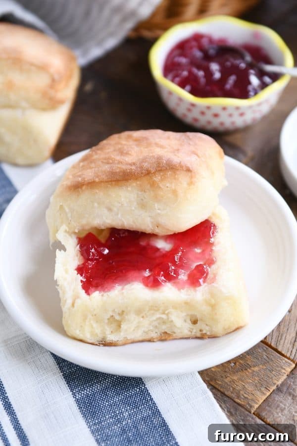 A fluffy dinner roll sliced in half, generously spread with butter and strawberry jam, highlighting its airy texture.