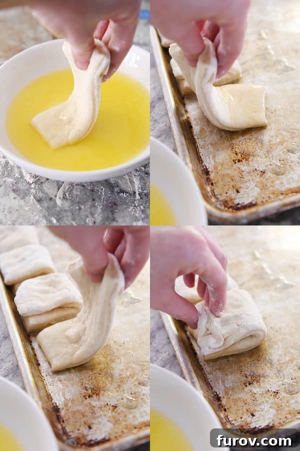 Dipping a rectangular piece of roll dough into melted butter and then folding it in half on a sheet pan, ready for baking.