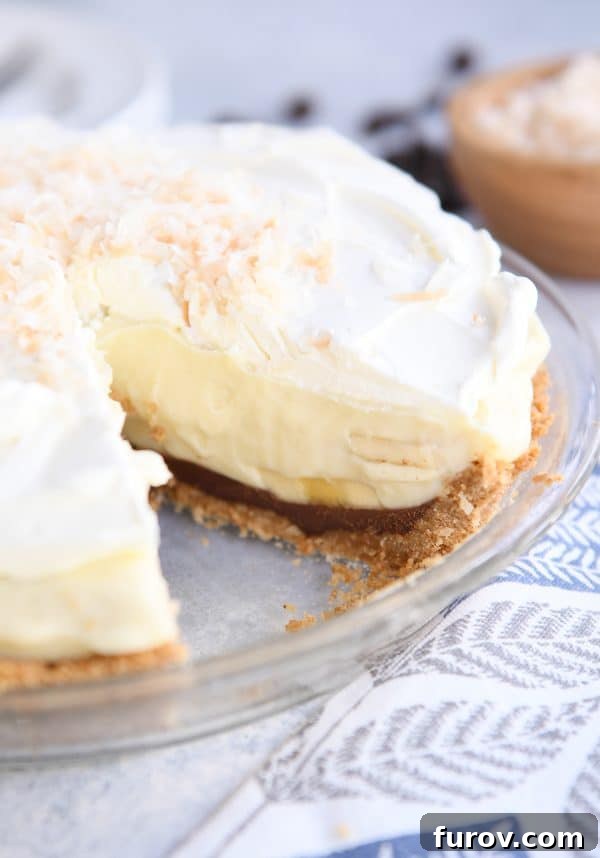 A whole Black Bottom Banana Coconut Cream Pie in a clear glass pie plate with one slice gracefully removed.