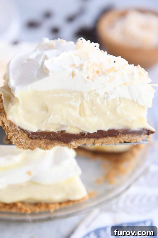 A slice of Black Bottom Banana Coconut Cream Pie elegantly placed on a silver pie server.