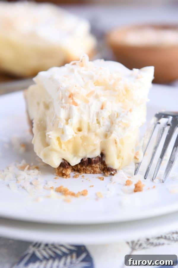 A delicious slice of Black Bottom Banana Coconut Cream Pie on a white plate with a bite already taken out, highlighting its luscious layers.