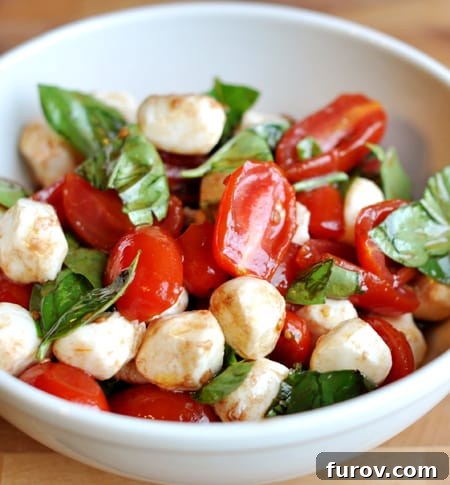 Vibrant Cherry Tomato Caprese 2 A beautiful white bowl filled with glistening mozzarella balls, vibrant halved cherry tomatoes, and fresh spinach leaves, all lightly drizzled with oil and ready to serve.