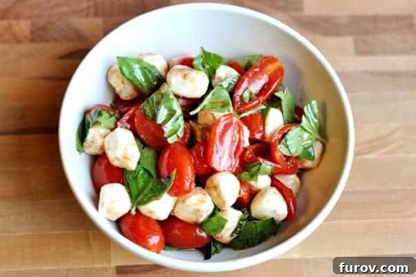 Vibrant Cherry Tomato Caprese 3 An overhead view of a vibrant Caprese salad in a white bowl, featuring perfectly sliced cherry tomatoes, small mozzarella balls, and fresh basil leaves, all glistening with a delicate dressing.