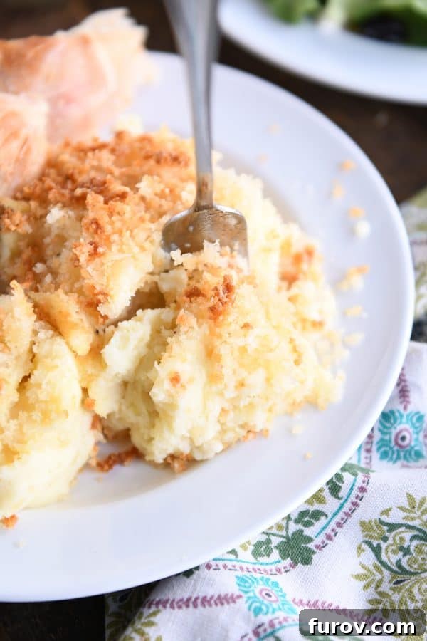 Fork scooping off part of creamy baked mashed potatoes on white plate.