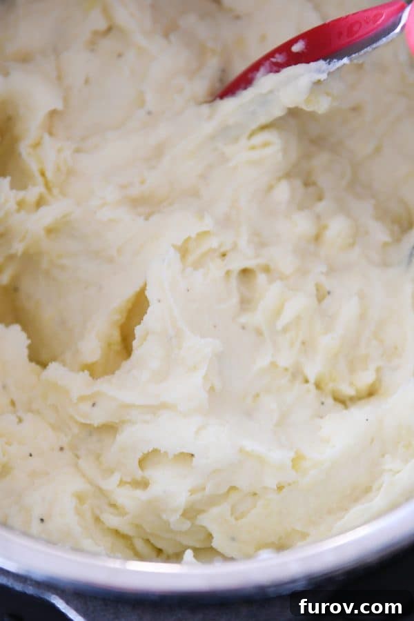 Creamy mashed potatoes in instant pot with potato masher.
