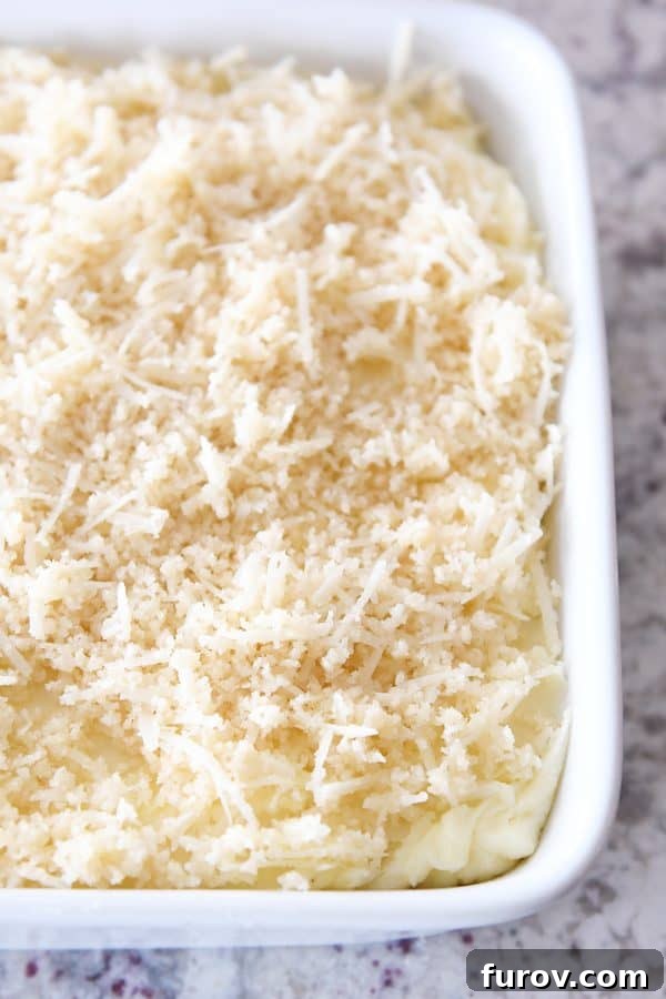 Mashed potatoes in white dish topped with buttery parmesan and bread crumb topping.