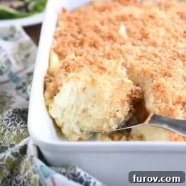 metal spoon scooping out spoonful of baked mashed potatoes with parmesan topping in white dish
