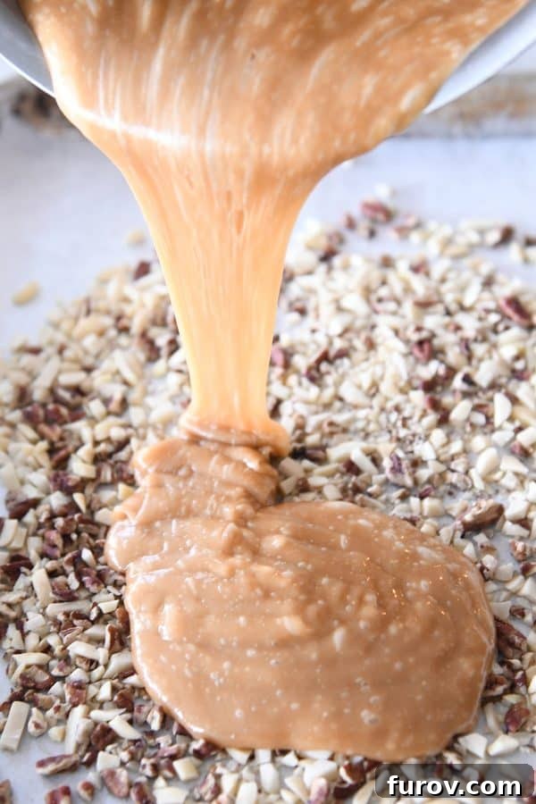Pouring hot homemade toffee over a layer of chopped nuts on a parchment-lined sheet pan.