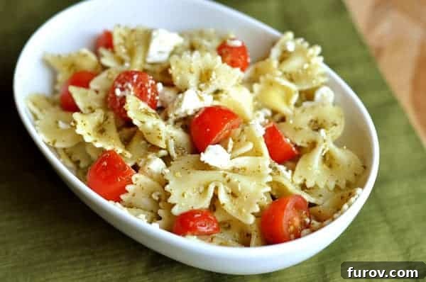 Vibrant Pesto Farfalle with Feta and Burst Tomatoes 2 White bowl full of cooked bowtie pasta, sliced cherry tomatoes, and crumbled feta cheese, garnished with fresh basil leaves.