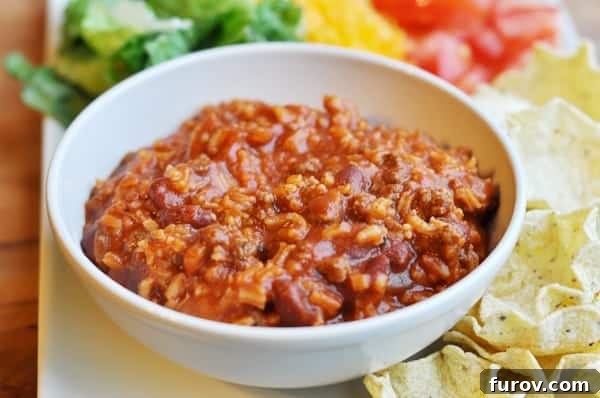 A beautifully presented white bowl of taco salad beef mixture, surrounded by an array of fresh toppings like crisp lettuce, shredded cheese, diced tomatoes, and crunchy tortilla chips, ready for dipping.