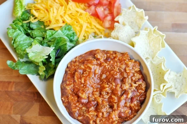 An overhead shot of a white bowl overflowing with the savory taco salad mixture, beautifully arranged with colorful toppings including fresh green lettuce, golden shredded cheese, vibrant red diced tomatoes, and crisp tortilla chips along the rim, inviting you to dip in.