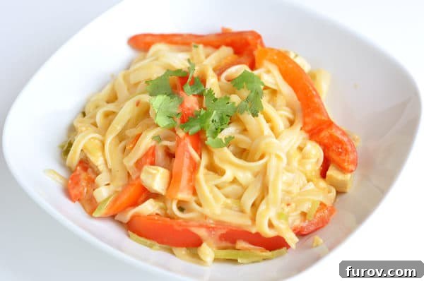 Close-up of a white bowl filled with Red Coconut Curry Noodles, featuring vibrant strips of red bell pepper and a rich, creamy sauce.