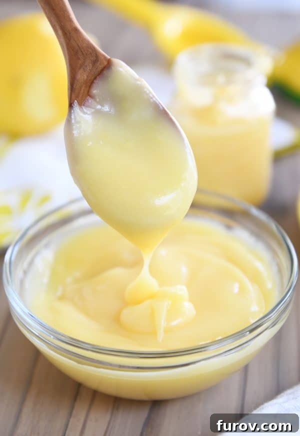 Bright and Zesty Instant Pot Lemon Curd 2 Wooden spoon dropping vibrant yellow lemon curd into a clear glass bowl, showcasing its smooth, rich texture.
