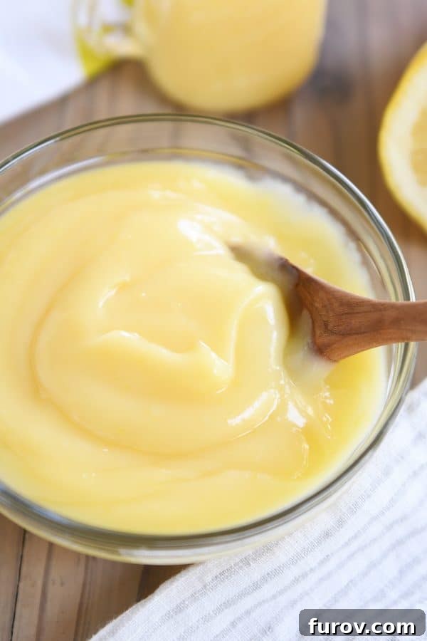Bright and Zesty Instant Pot Lemon Curd 3 A glass bowl brimming with creamy Instant Pot lemon curd, accompanied by a wooden spoon, against a rustic backdrop.