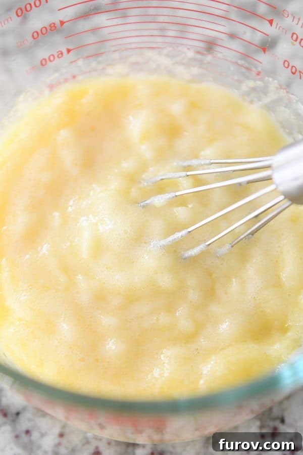 Bright and Zesty Instant Pot Lemon Curd 6 A hand vigorously whisking a lumpy, freshly cooked Instant Pot lemon curd in a clear glass bowl, just before its creamy transformation.