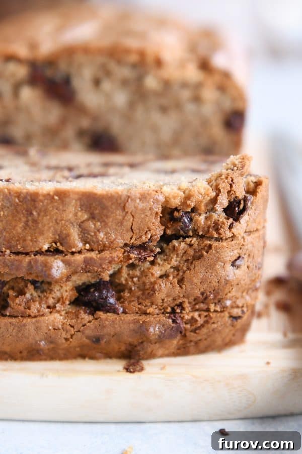 Three slices of peanut butter banana bread stacked on wood cutting board.