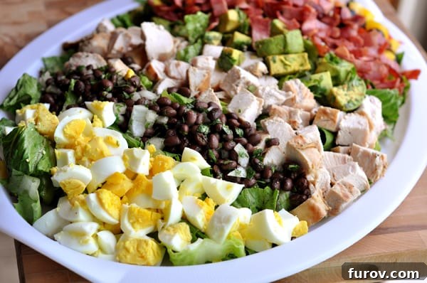 Fiesta Cobb with Bright Green Goddess Dressing 3 Close-up of chopped ingredients including egg, black beans, chicken, bacon, and avocado on a white platter, ready for assembly.