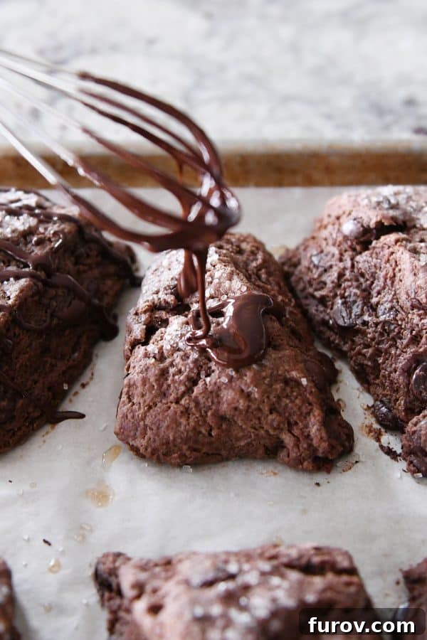 Chocolate glaze being drizzled from a whisk onto baked chocolate scones.