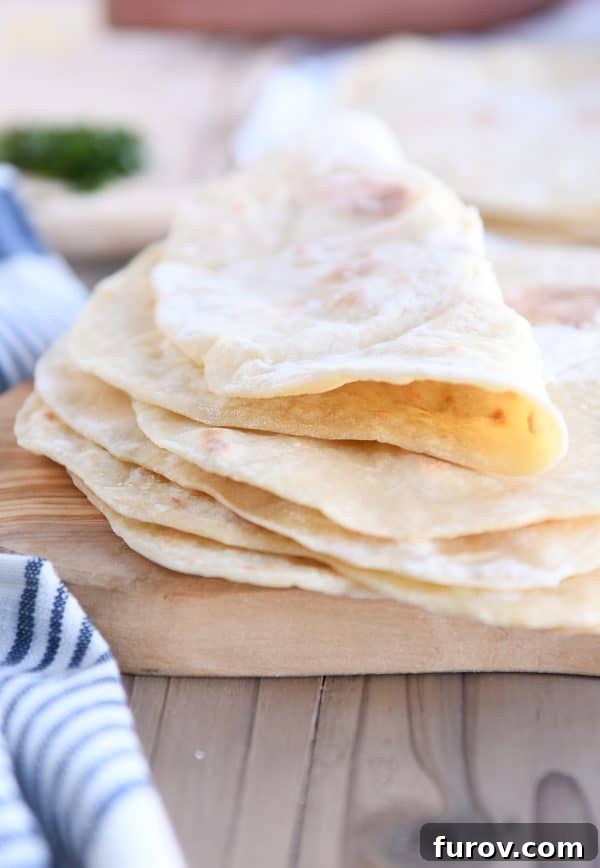 Folded piece of yogurt flatbread on stack of four flatbreads, showcasing its soft texture and golden spots.