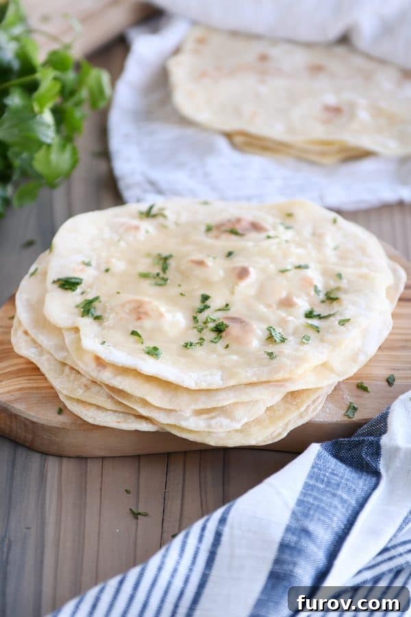 Stack of freshly cooked yogurt flatbreads on a wooden cutting board, garnished with chopped parsley, inviting to be enjoyed.