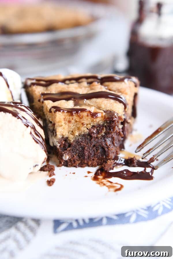 A delectable slice of brookie pie, showing its distinct brownie and cookie layers, served on a white plate with a spoonful missing and a scoop of vanilla ice cream melting alongside.