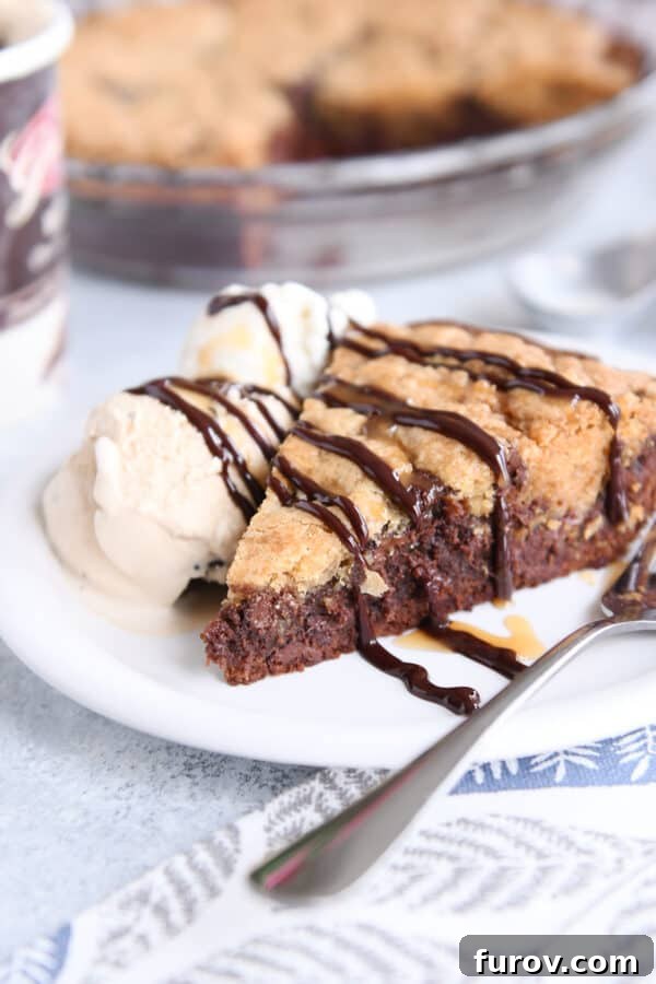 A tantalizing slice of brookie pie sits on a pristine white plate, accompanied by a fork and a melting scoop of ice cream, ready to be enjoyed.