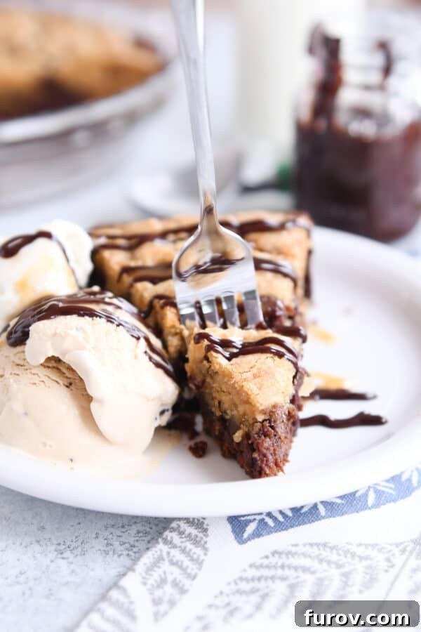 A fork is poised to take a bite from a slice of brookie pie, highlighting the inviting texture and irresistible appeal of the dessert on a white plate.